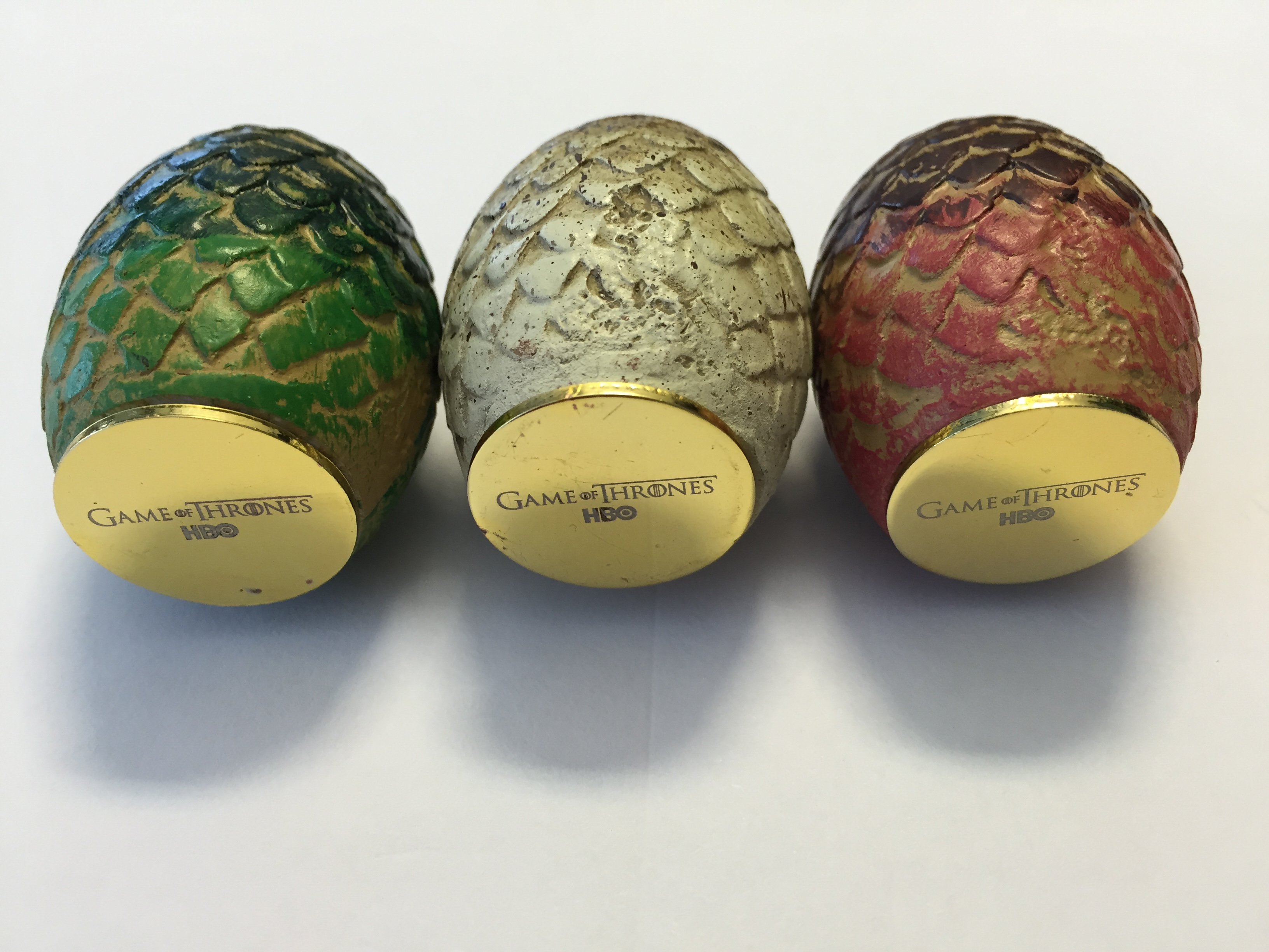 Drei Game of Thrones Dracheneier. Grün, weiß und rot. Goldene Basen. Weißer Hintergrund.