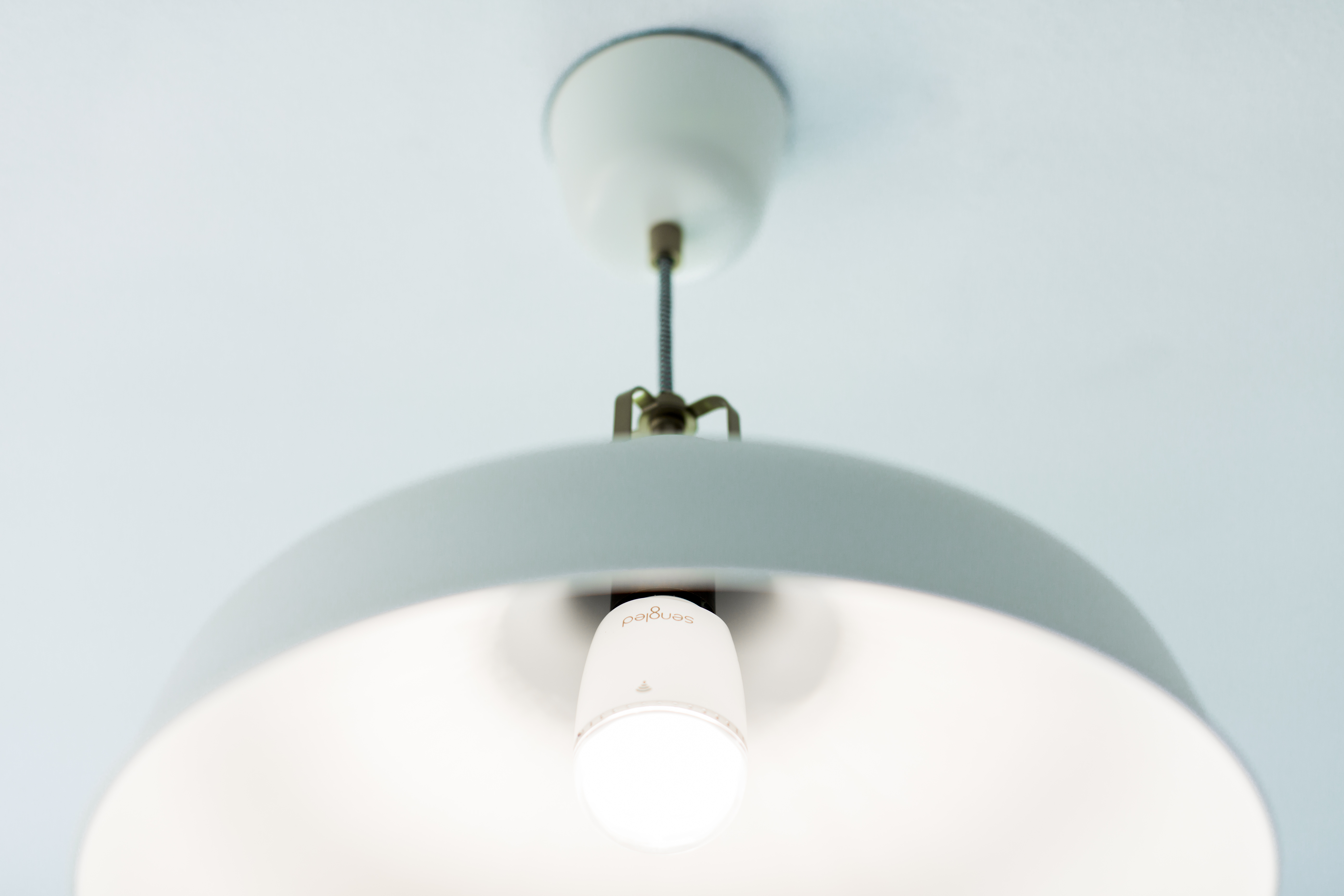 A white, modern pendant light hangs from a light blue ceiling. The light is on and illuminates the room.
