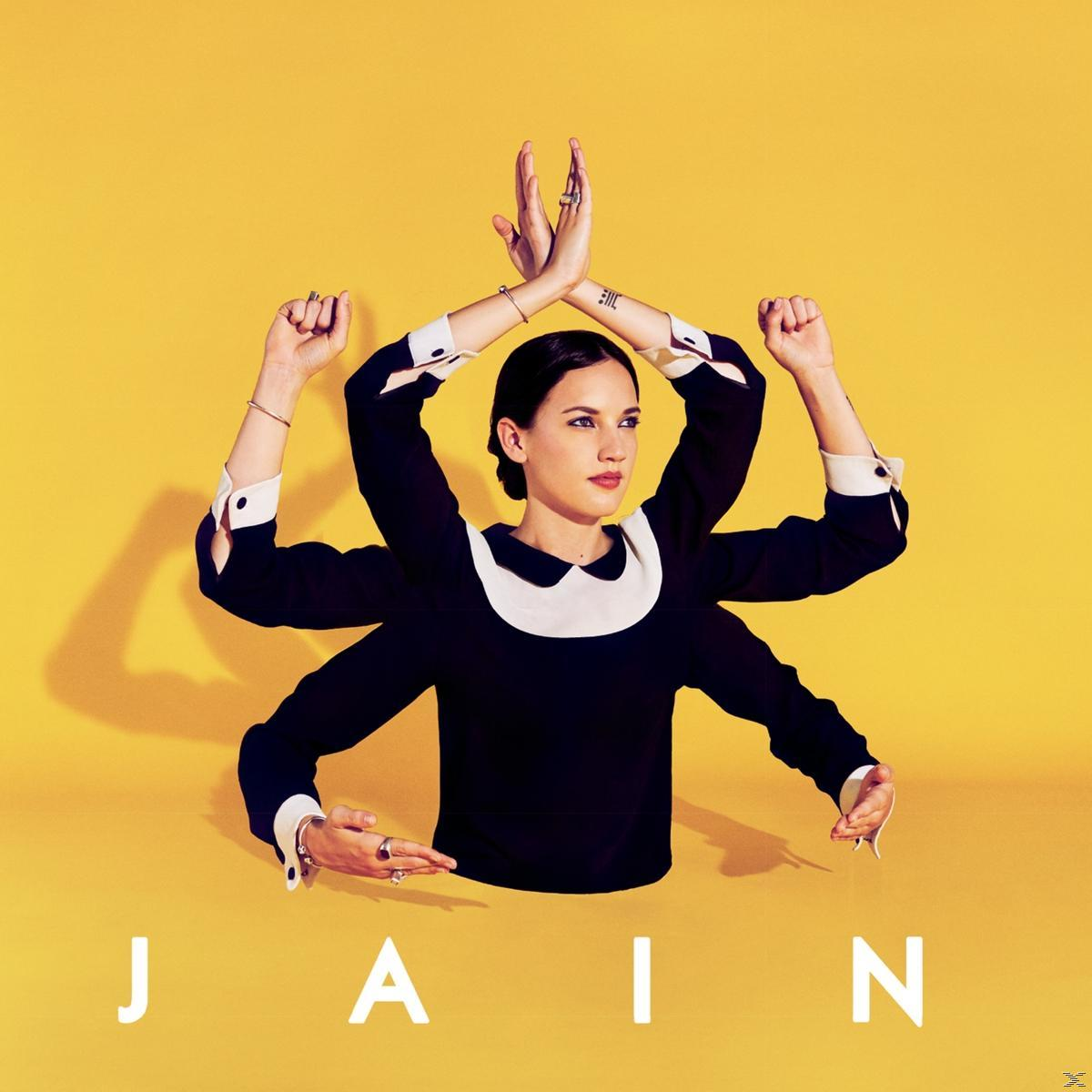 Pochette d'album de JAIN avec une femme en robe noire sur fond jaune, les bras levés.