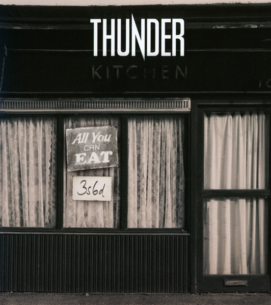 Ein Geschäft mit Fenstern, Schilder sagen 'Thunder Kitchen' und 'All You Can Eat'. Das Gebäude ist schwarz und weiß.