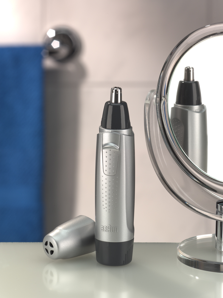 Silver nose hair trimmer with a black head, next to a mirror. White background.