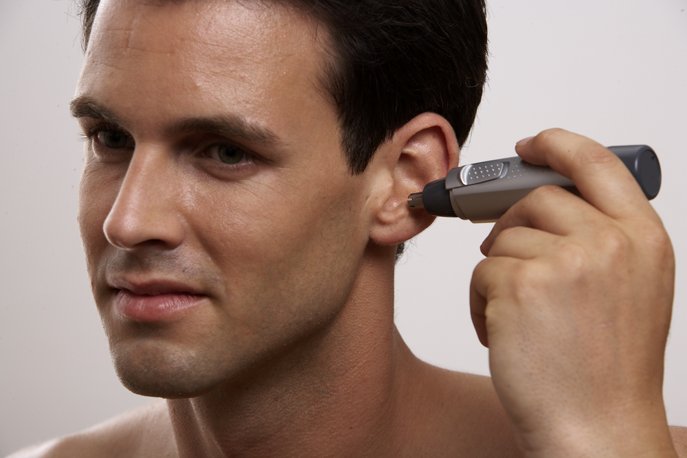 A man using a nose and ear hair trimmer. The trimmer is gray and black. The man has dark hair.