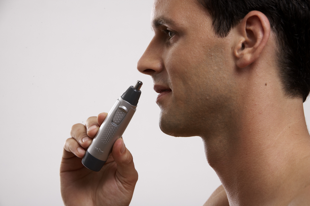 A man is using a nose hair trimmer, holding it to his nose.