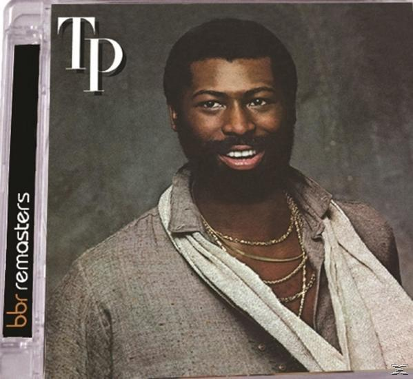 Szakállas férfi aranyláncokkal, szürke inget visel. TP Remasters logó.