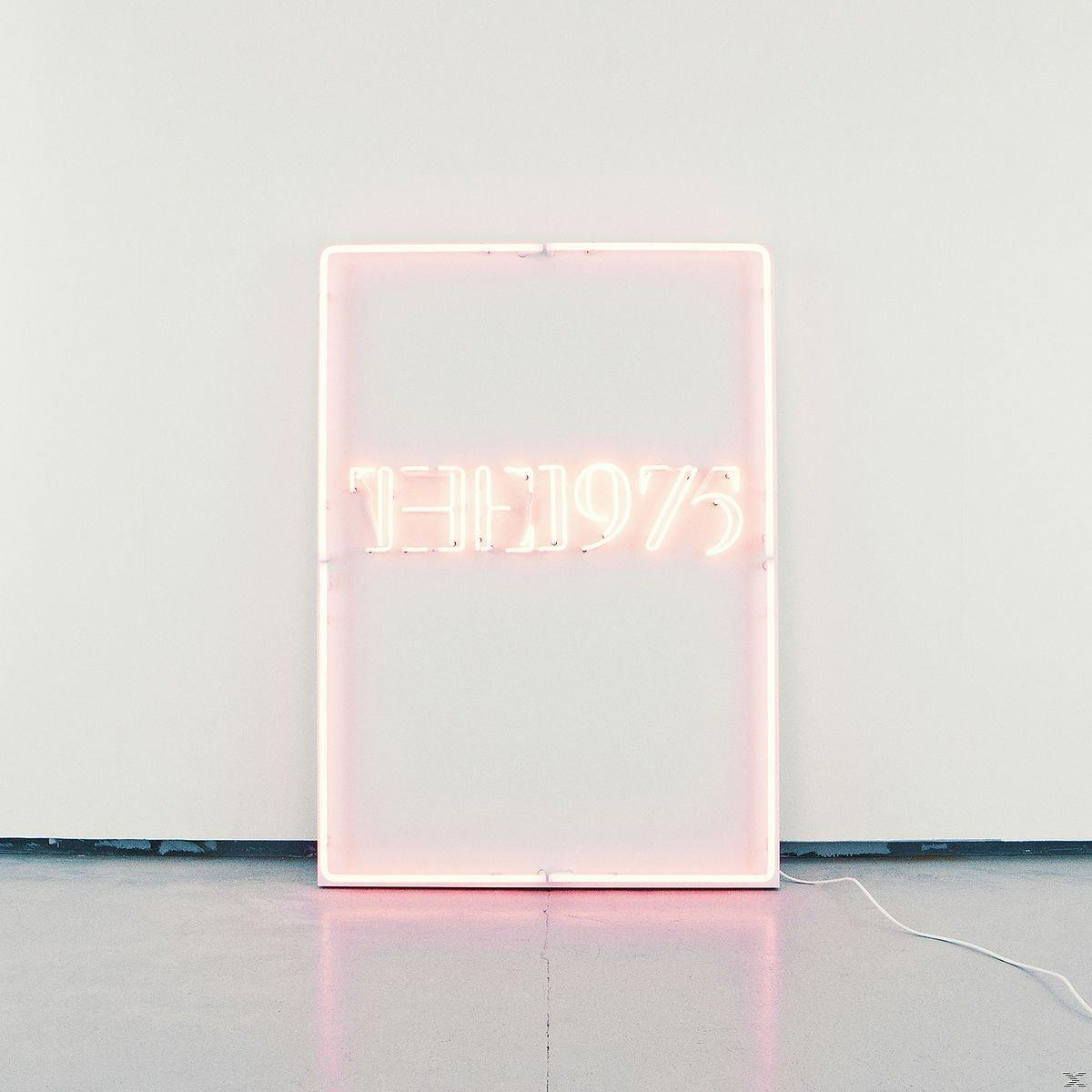 "THE1975" feliratú neonfény egy fehér falon és szürke padlón.