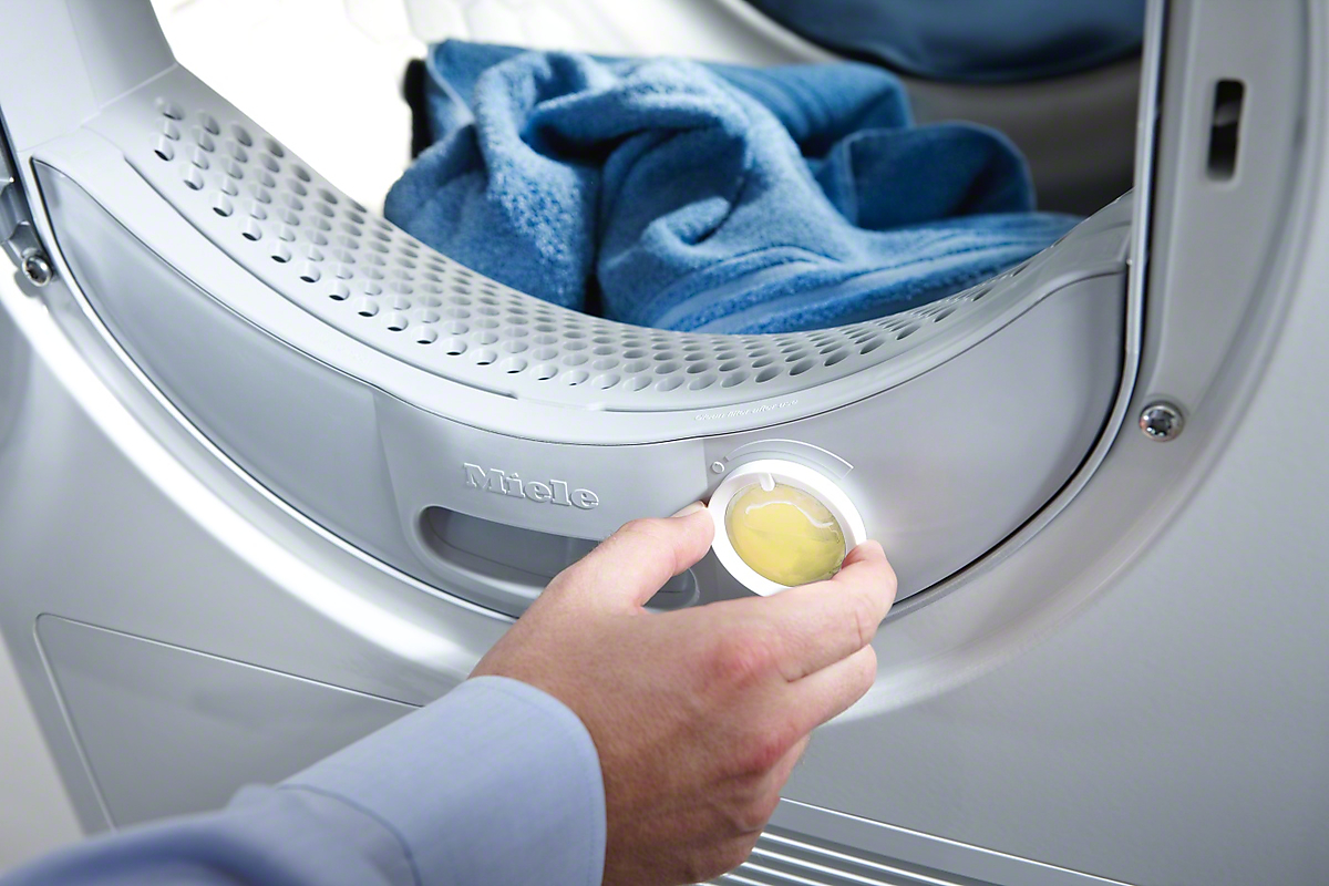 A hand turns a dial on a Miele dryer with blue towel inside.