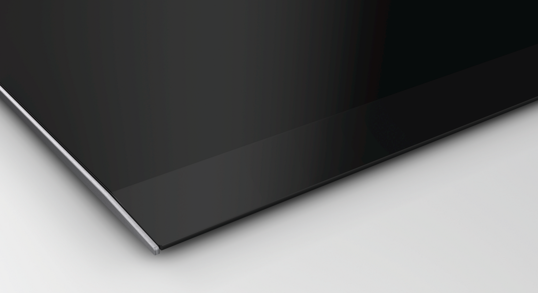 Gros plan d'une table de cuisson en verre noir avec bord métallique sur fond blanc.