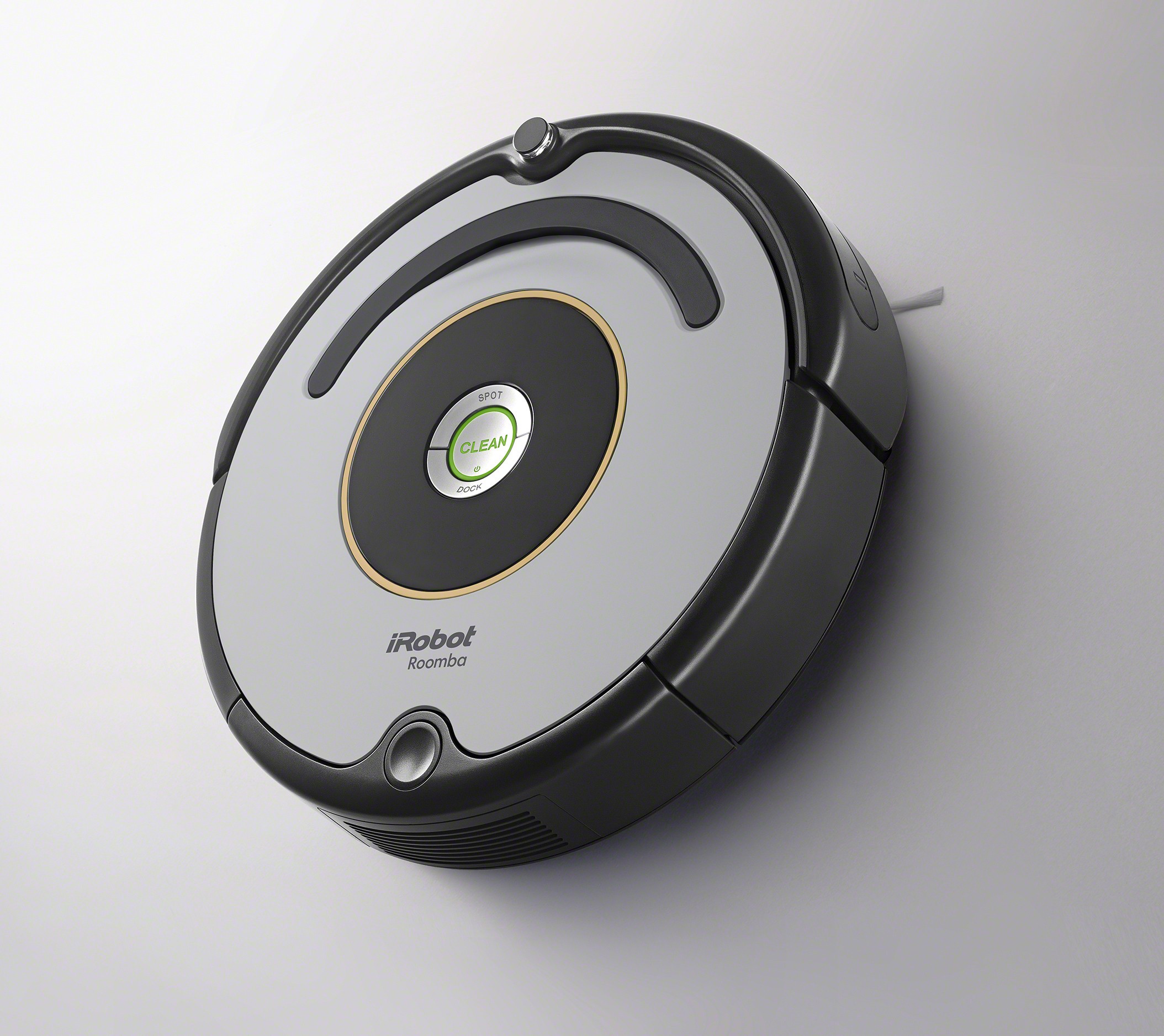Ein iRobot Roomba Staubsauger. Er ist schwarz und silberfarben mit einem zentralen Knopf. Der Hintergrund ist eine hellgraue Wand.