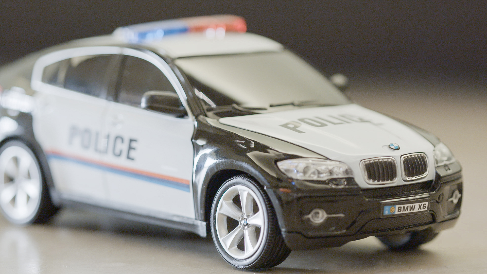 Spielzeug-Polizeiauto, schwarz und weiß, mit blinkenden Lichtern, im Fokus. Verschwommener Hintergrund.