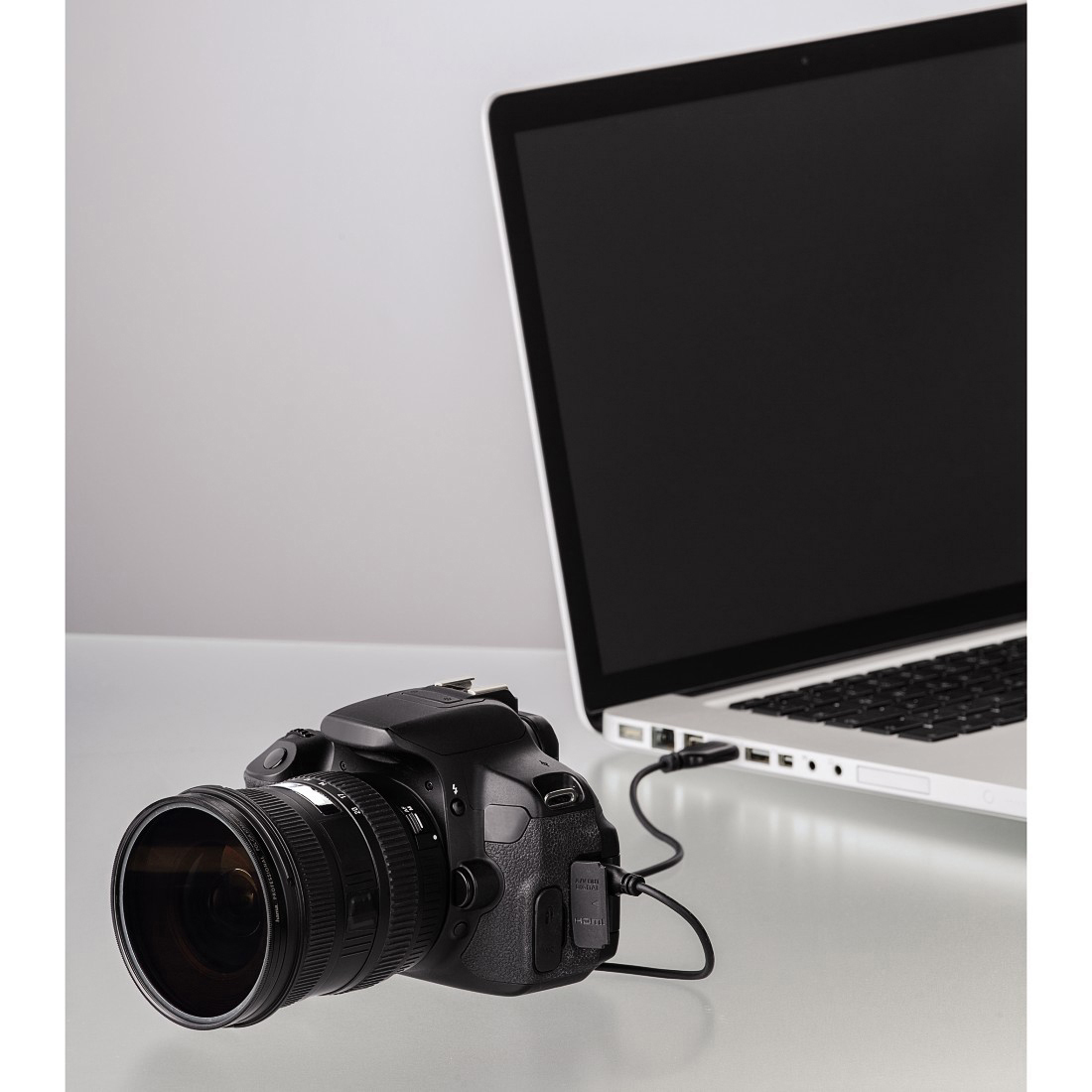 Appareil photo reflex numérique connecté à un ordinateur portable avec un câble. L'ordinateur portable est ouvert sur une surface blanche.