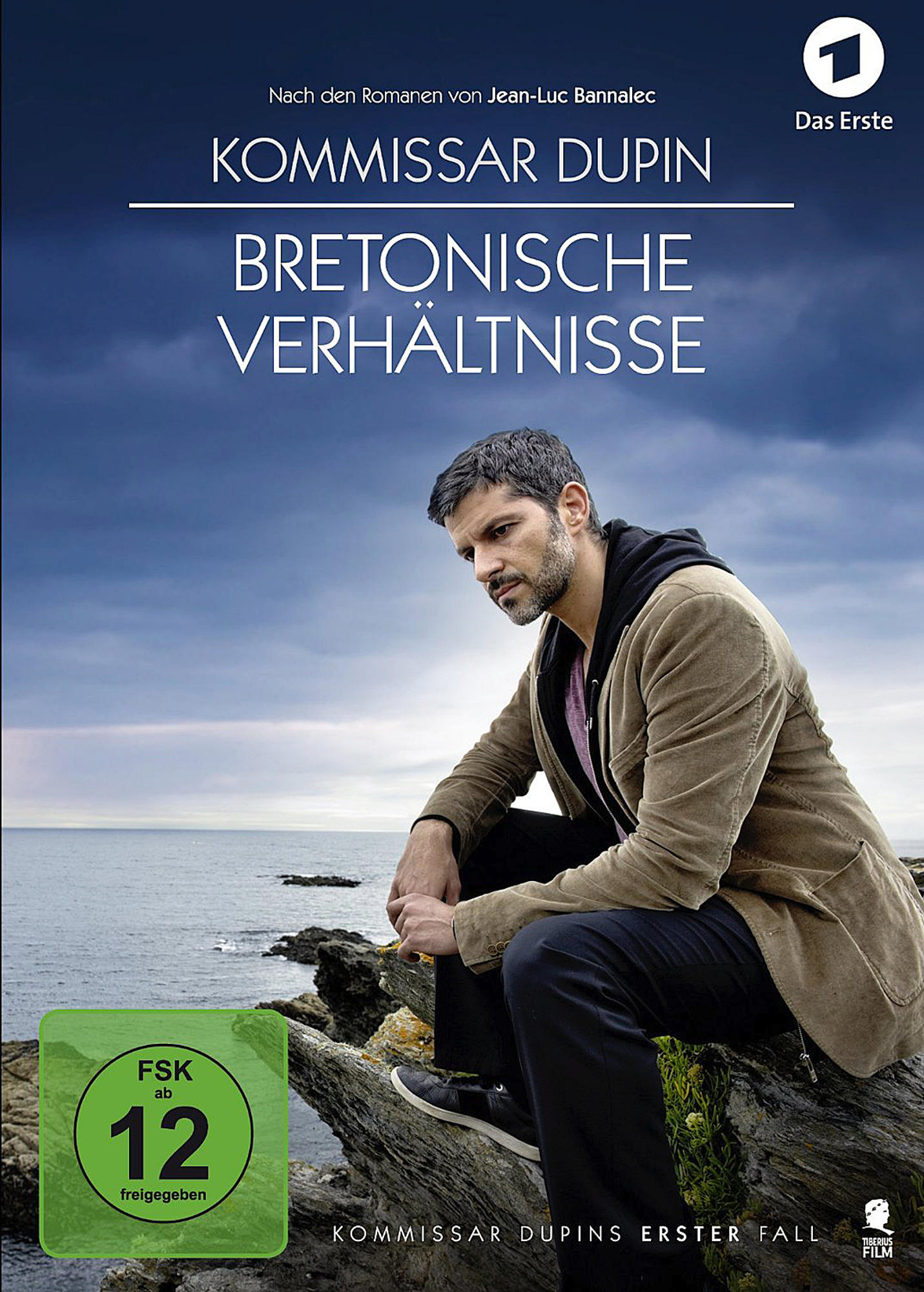 Mann sitzt auf Felsen am Meer und wirkt nachdenklich. Ein Filmplakat ist sichtbar, Text auf Französisch.