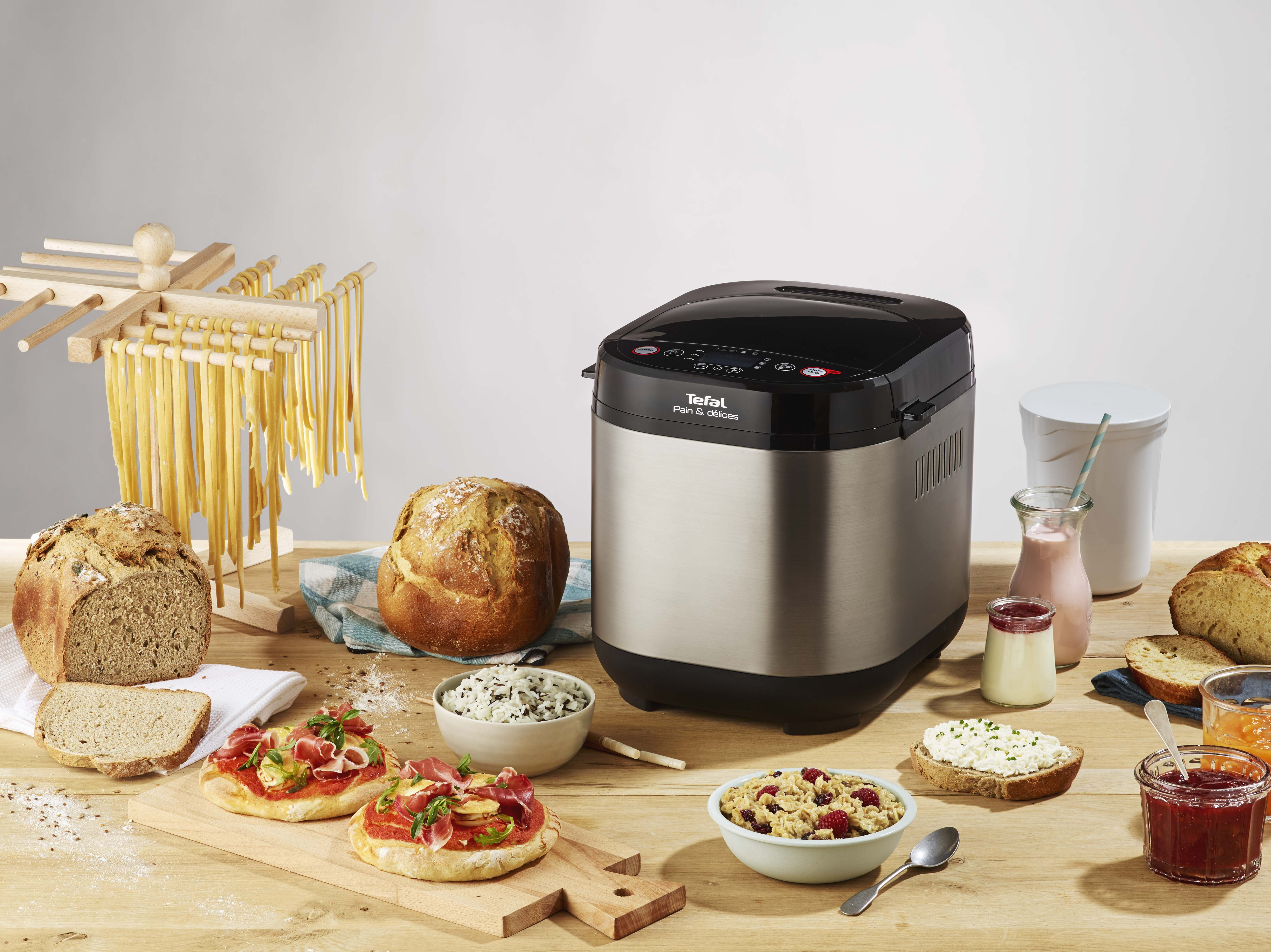 Een broodbakmachine met brood, sneetjes brood en toppings op een houten tafel.