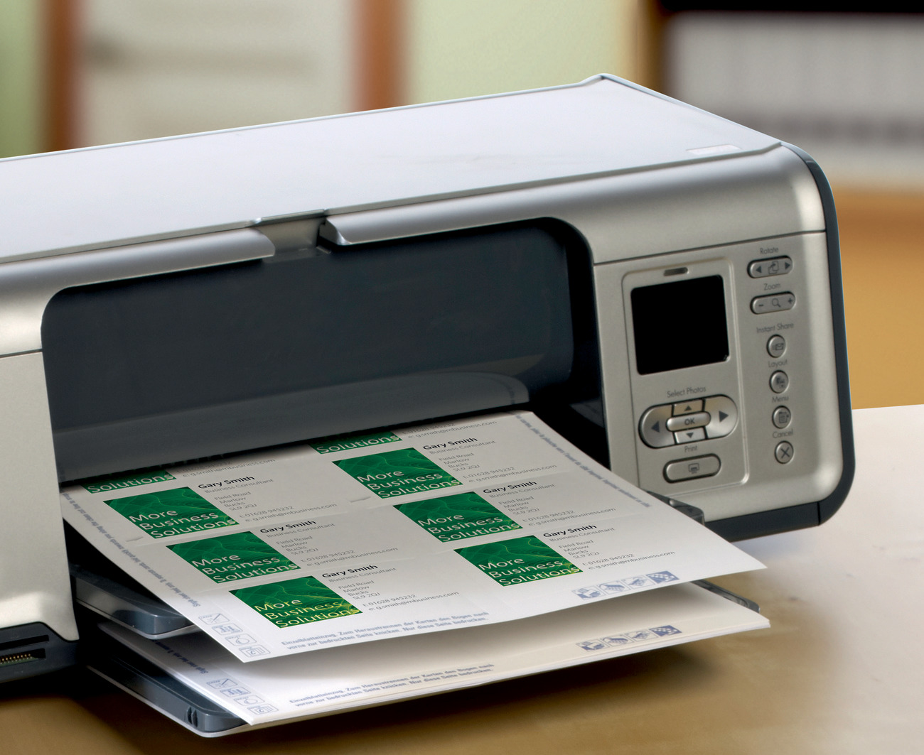 Ein Drucker druckt Visitenkarten. Die Karten haben ein grünes Logo und Text. Der Drucker ist silberfarben.