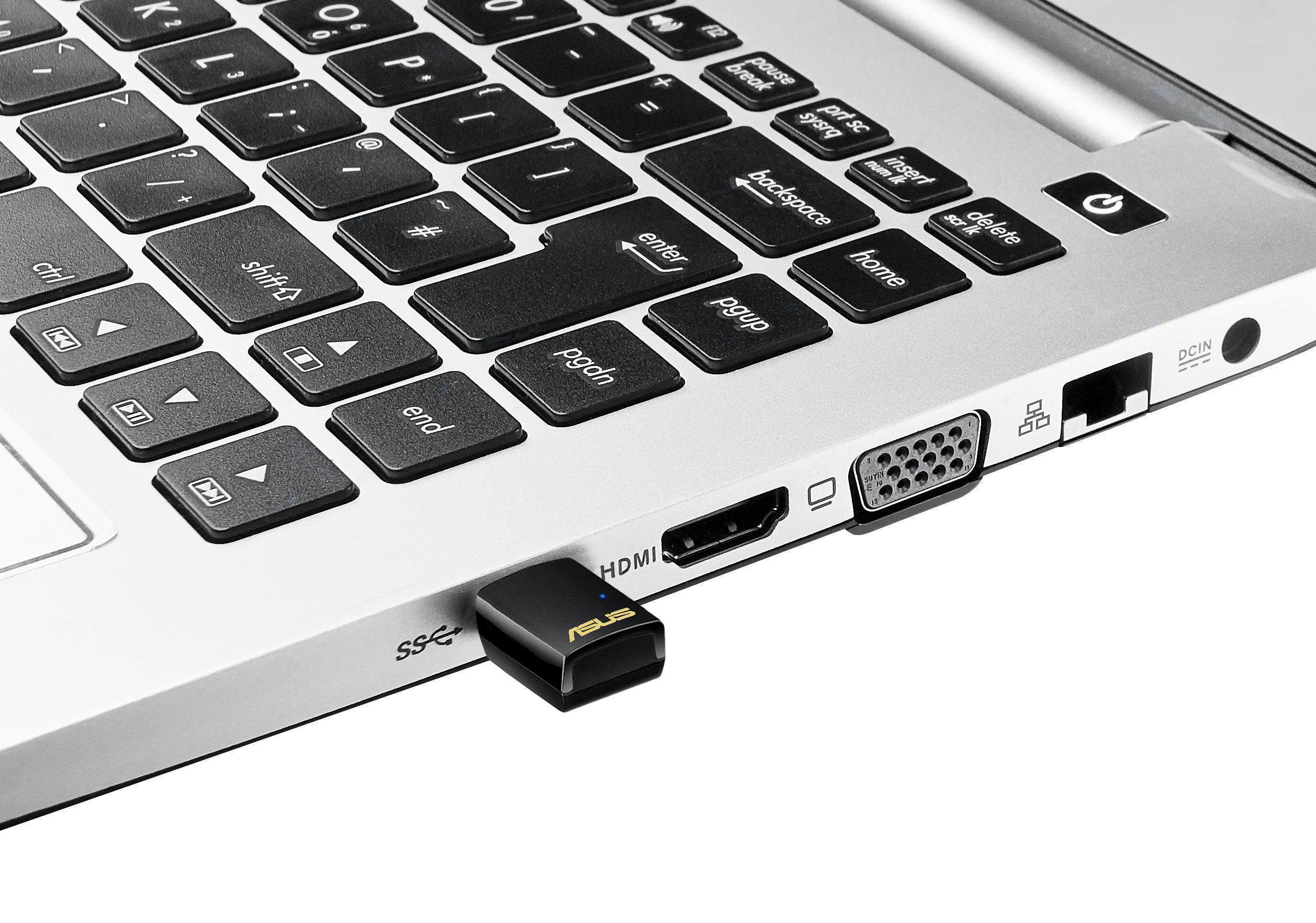 Ein schwarzer USB-Adapter, der in einen silbernen Laptop eingesteckt ist. Der Adapter hat das ASUS-Logo.