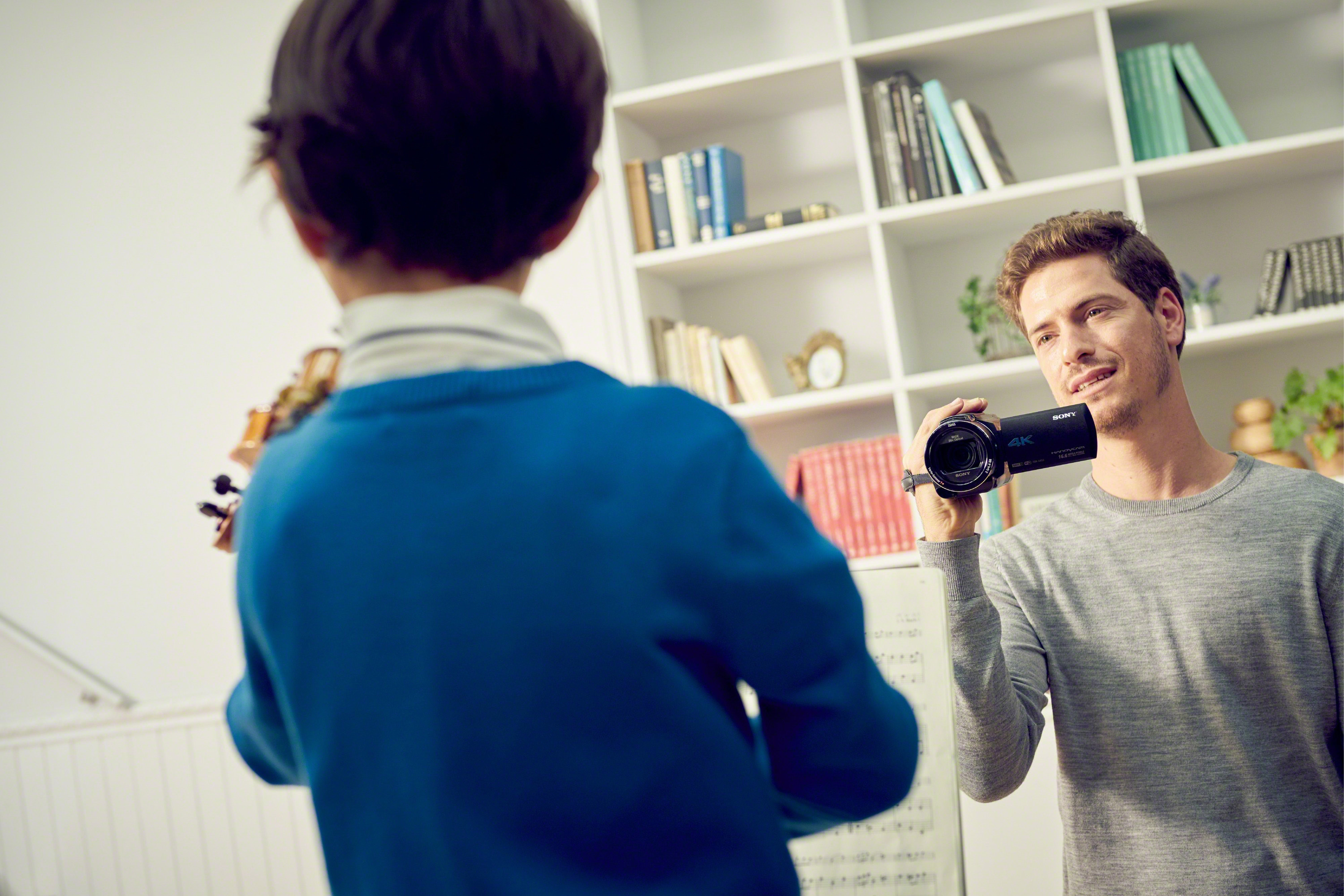 Un uomo che filma un bambino che suona il violino in una stanza.