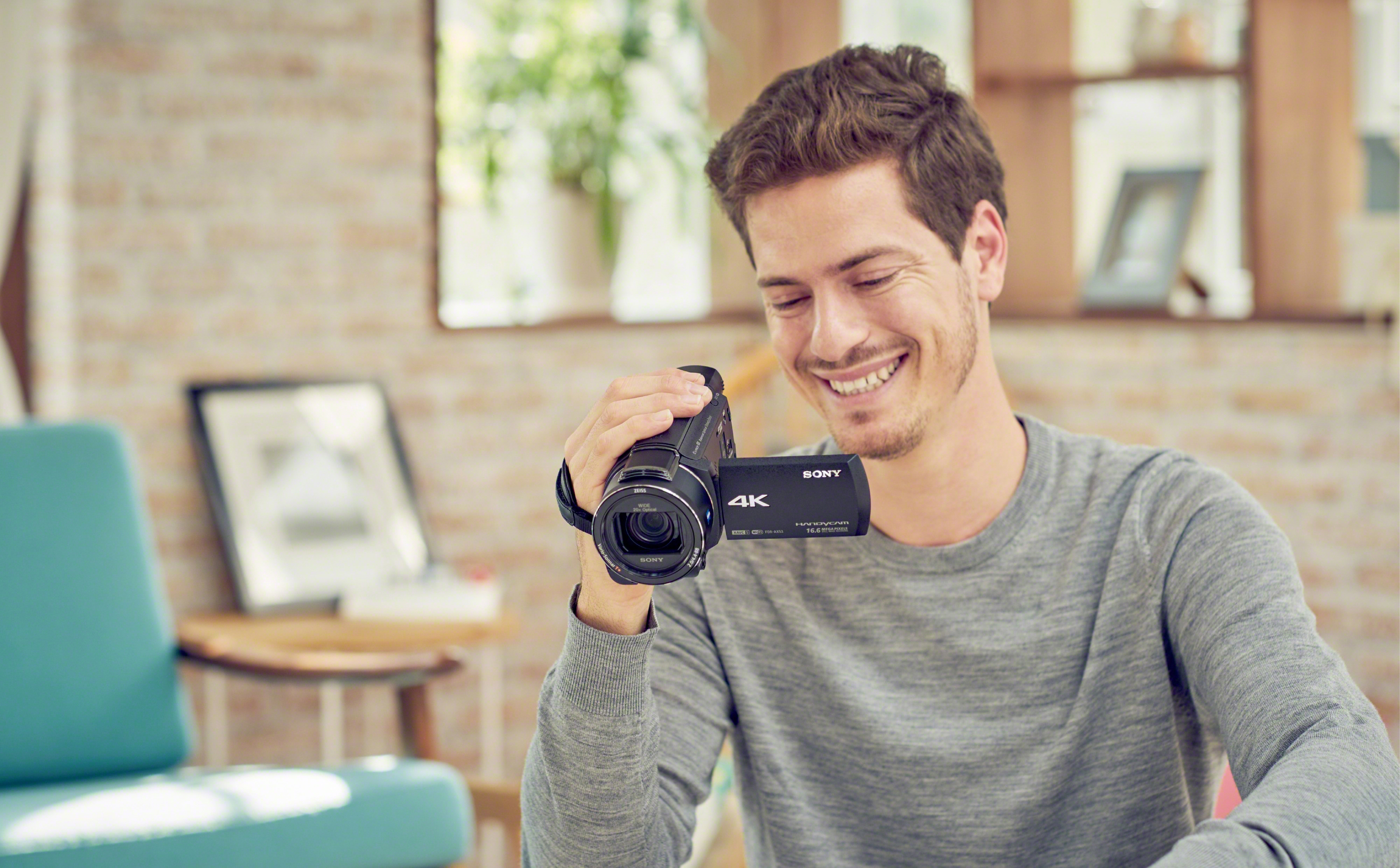 Uomo sorridente che tiene una videocamera Sony nera, seduto in una stanza luminosa.