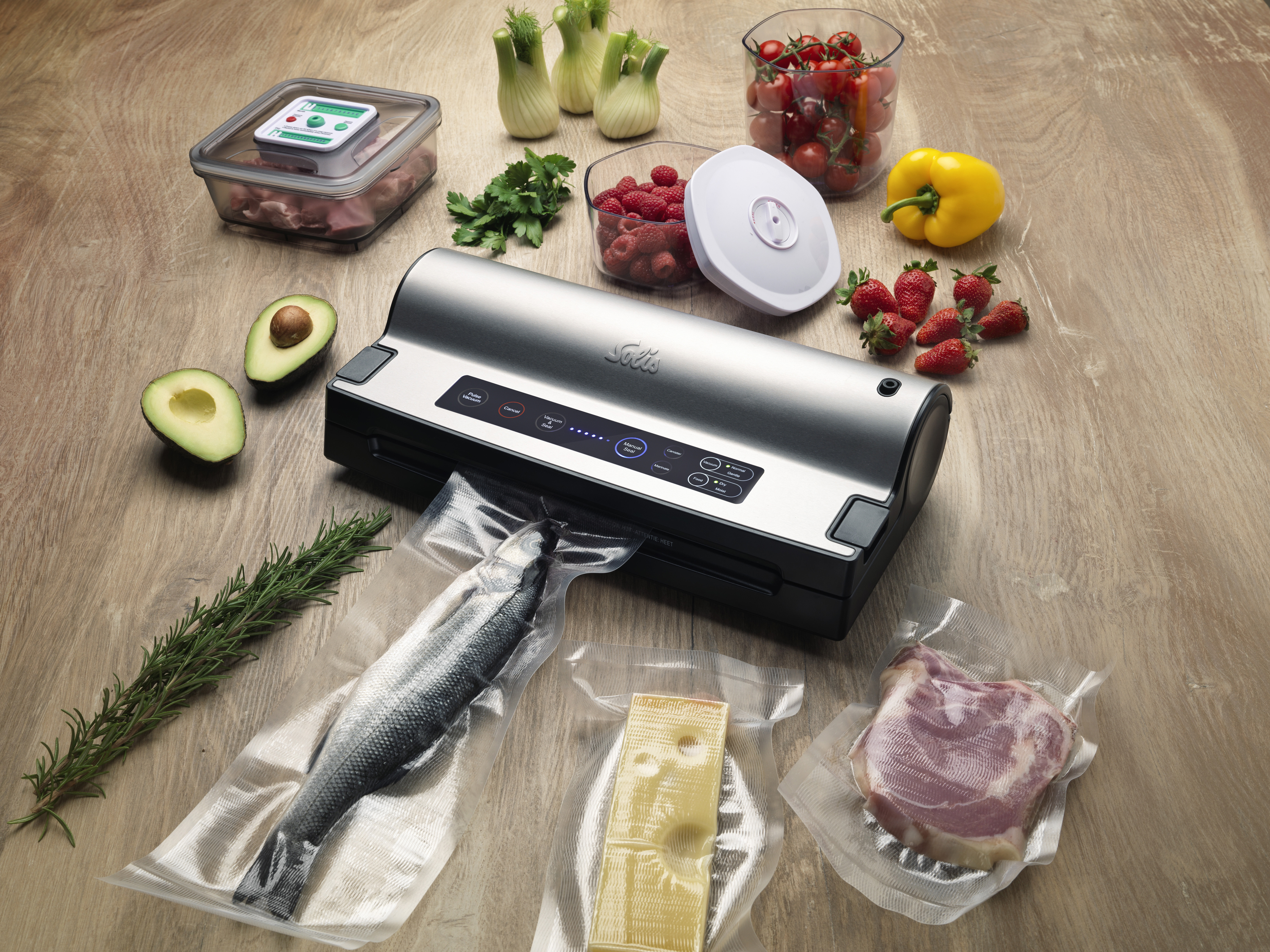 Een vacuümmachine met voedingsmiddelen zoals vis, vlees, kaas, fruit en groenten op een houten tafel.