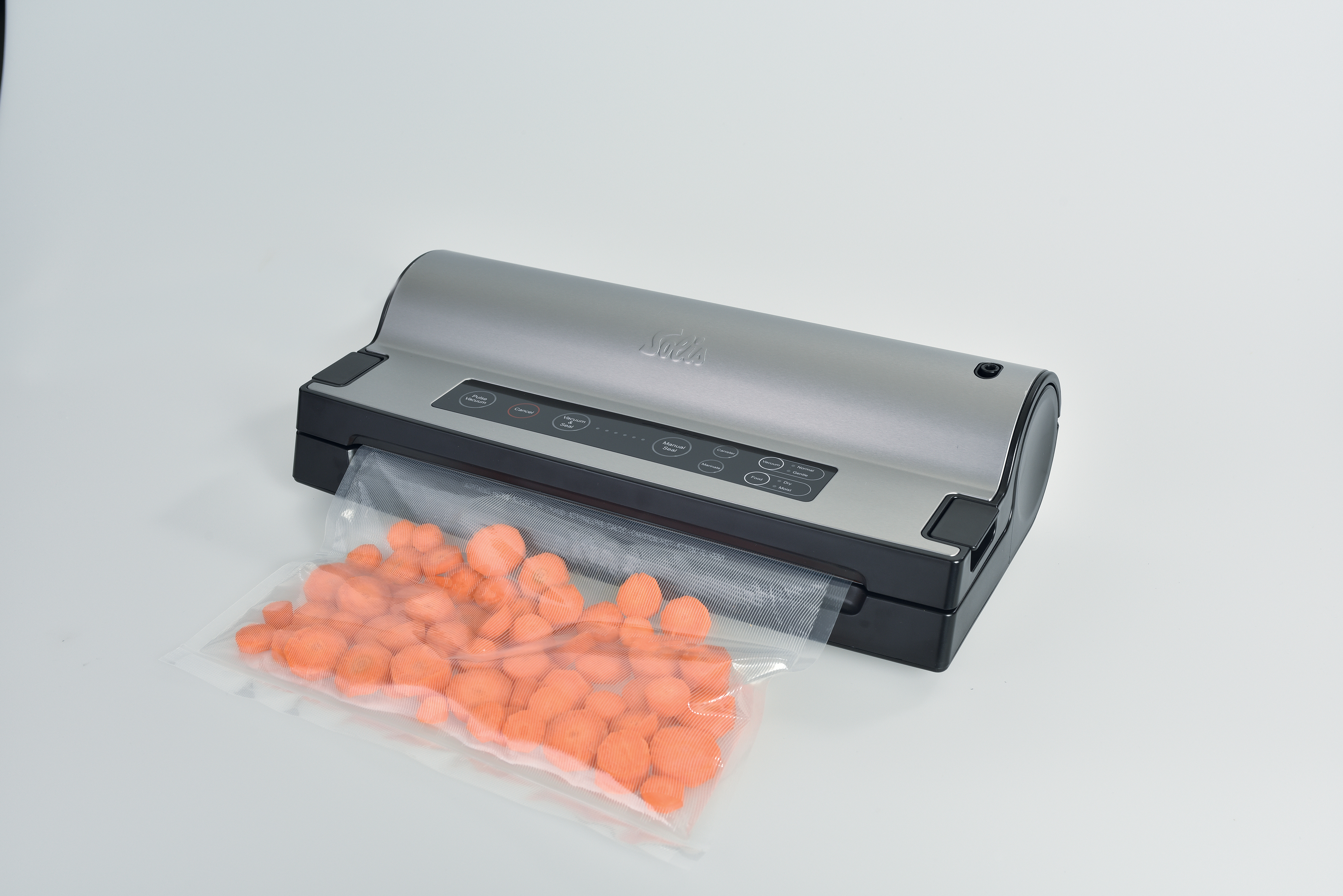 Een vacuümmachine met een zakje oranje wortelschijfjes. De sealer is grijs en zwart. Witte achtergrond.