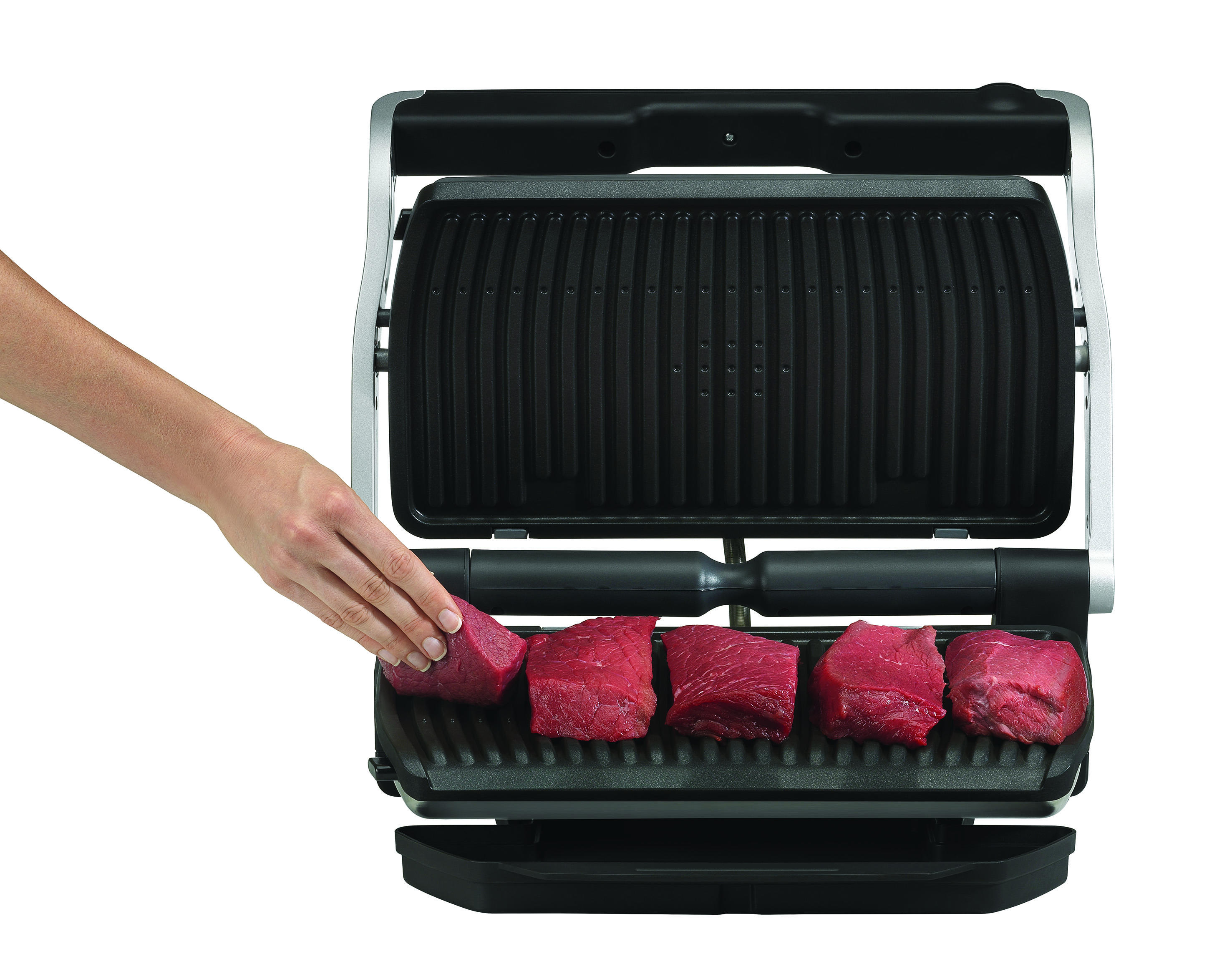 Eine Hand legt rohes Fleisch auf einen Grill. Der Grill ist geöffnet und hat Rillen. Weißer Hintergrund.