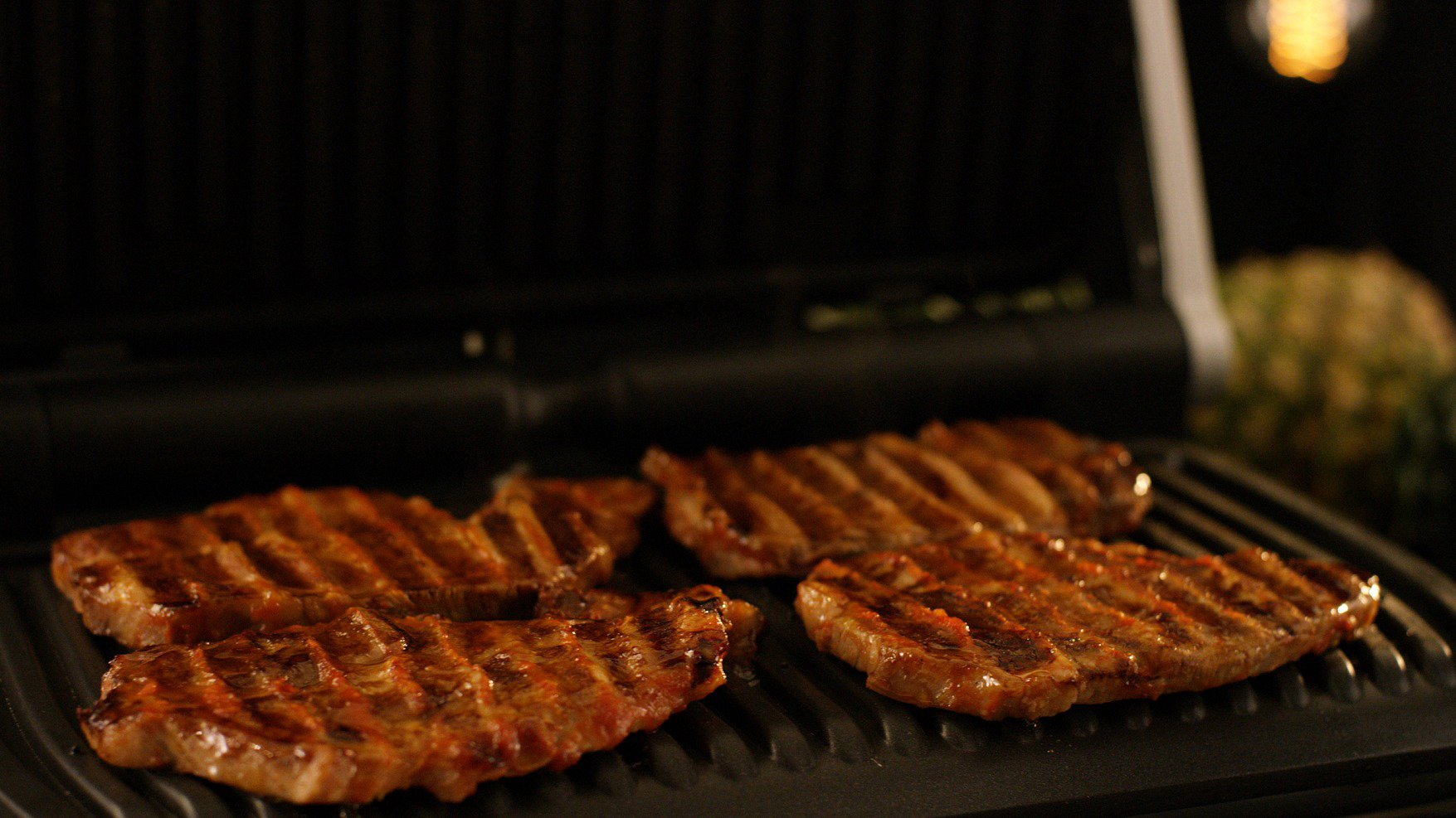 Vier gegrillte Steaks auf einem heißen Grill, Grillspuren sichtbar.