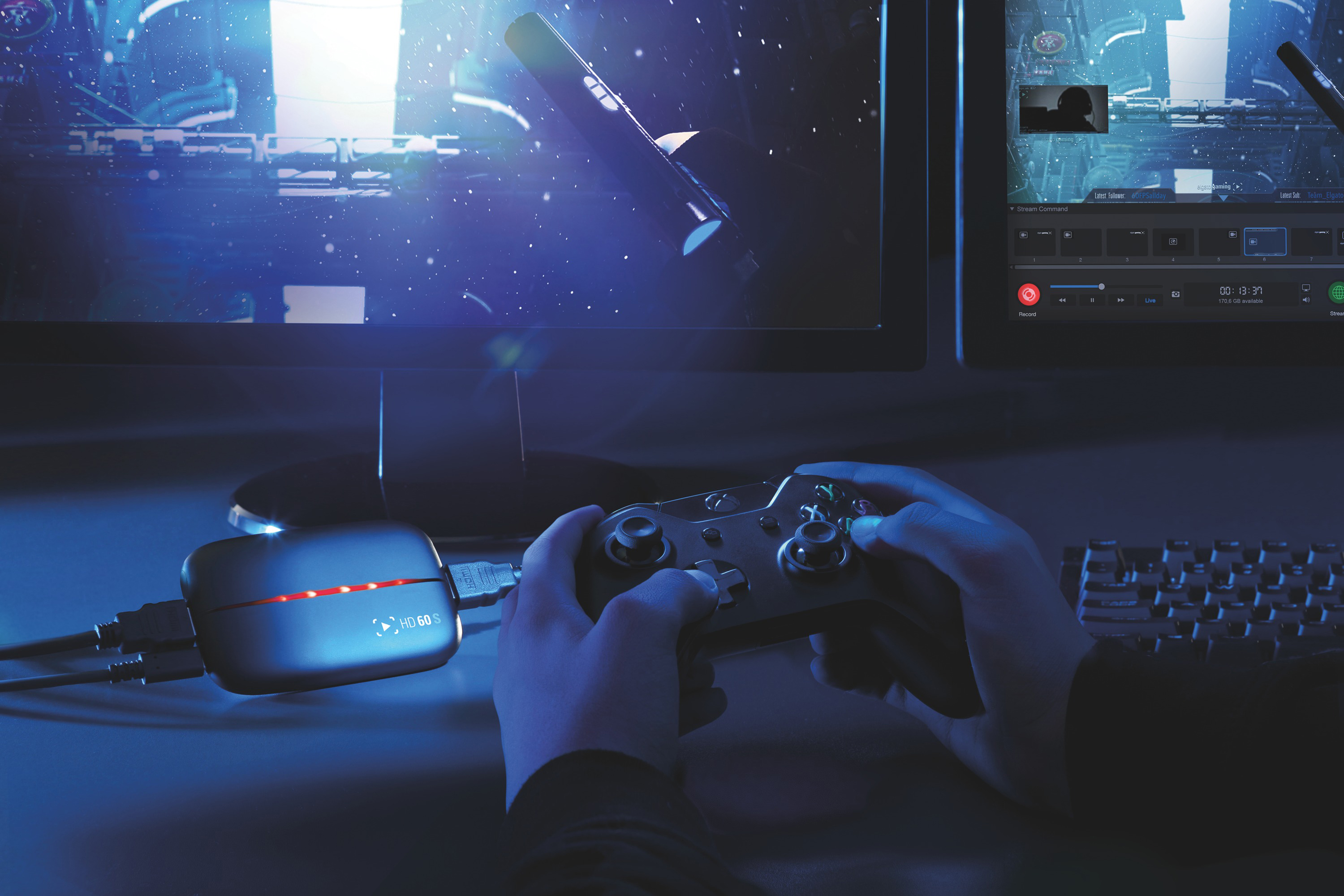 Eine Person spielt ein Videospiel. Auf dem Schreibtisch befinden sich zwei Monitore und ein Gamecontroller.