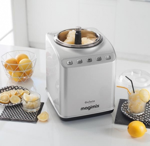 Machine à glace argentée sur une surface blanche. Citrons, verres et un bol à proximité.
