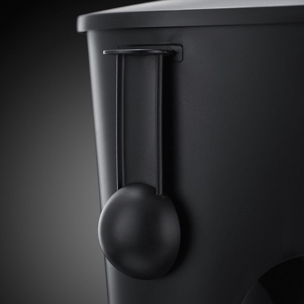A black plastic scoop hanging on the side of a black container.