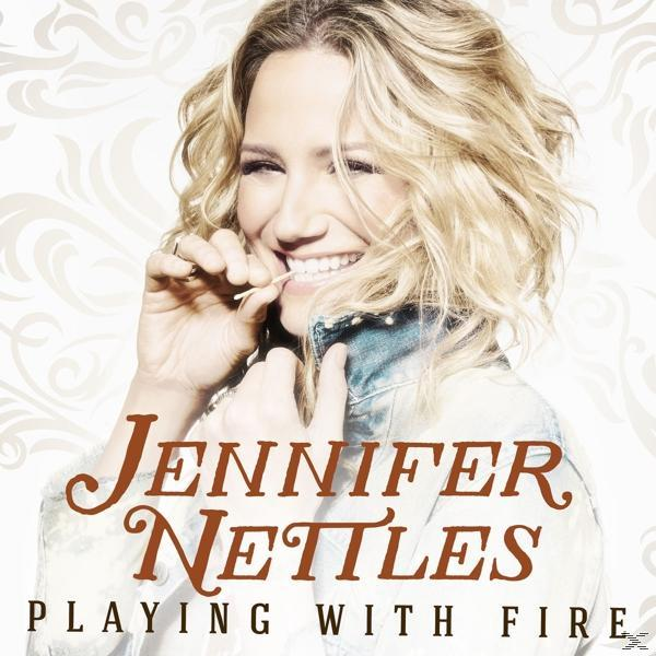 Albumcover: Jennifer Nettles, 'Playing with Fire'. Frau mit blonden Haaren, lächelnd, hält einen Zahnstocher.