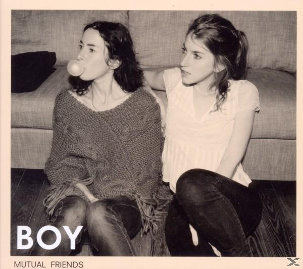 Zwei junge Frauen sitzen auf dem Boden. Eine bläst Kaugummi, die andere schaut zu. Couch im Hintergrund. Schwarz-Weiß-Foto.