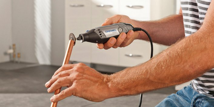 Személy Dremel szerszámmal vág egy rézcsövet. A kezek fókuszban vannak.