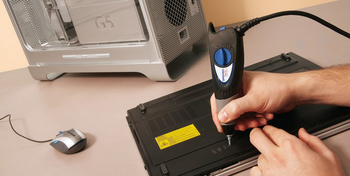 Egy személy egy Dremel szerszámot használ egy laptopon. A laptop nyitva van egy asztalon.