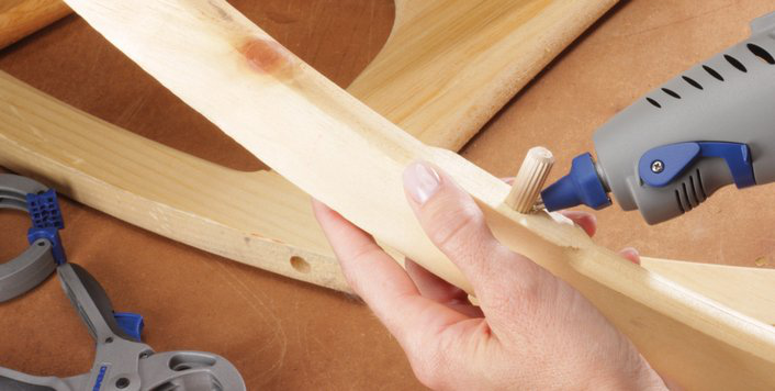 Közelkép: személy Dremel szerszámot használ fán, széket szerel.