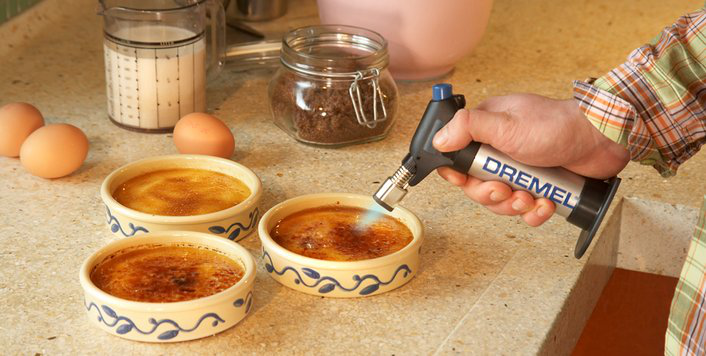 Egy személy Dremel fáklyát használ a cukor karamellizálásához a crème brûlée-n.