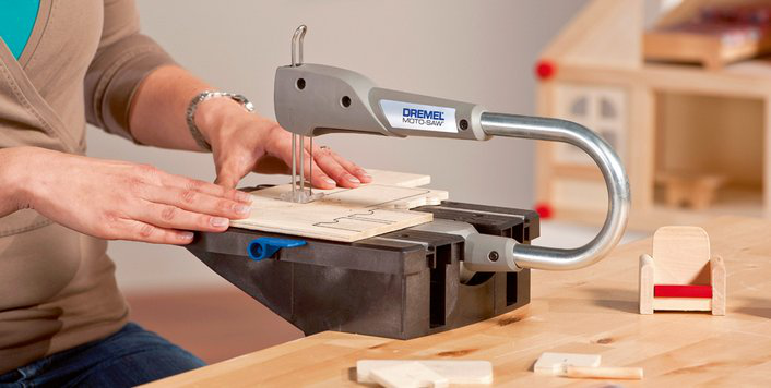 Nő Dremel Moto-Saw-val fát vág. Babaház és bútorok a háttérben.