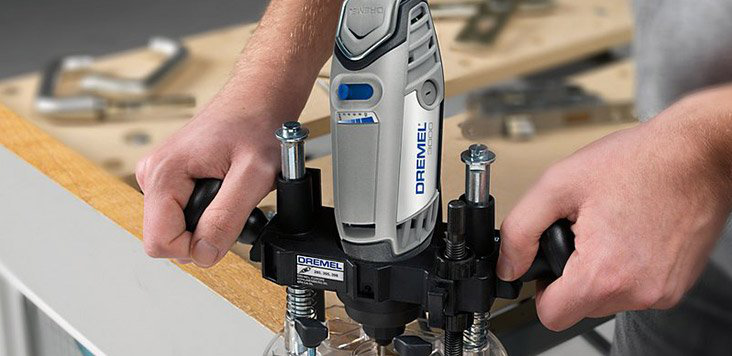 Egy férfi Dremelt használ egy darab fa kivágásához. A Dremel fekete és szürke.