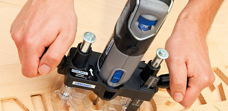 Egy személy Dremel forgó szerszámot használ egy fa felületen, a szerszám egy sablonban.
