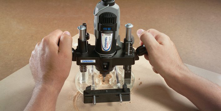 Egy személy Dremel-t használ a fa faragásához. A szerszám rögzített, a kezekkel működtetik.