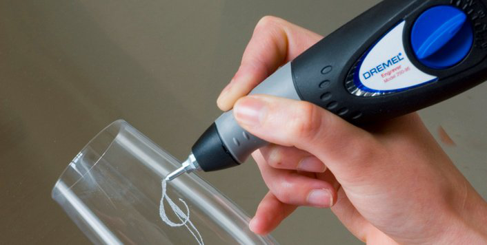 Kéz Dremel Engraver szerszámot használ üvegre mintát gravírozáshoz. Közeli kép, szürke és fekete szerszám.