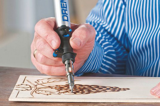 Egy személy Dremel szerszámot használ egy fa deszkára szőlő mintát gravírozni.