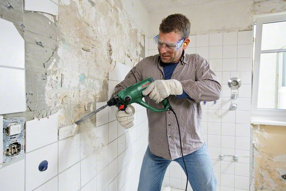 Szemüveget és kesztyűt viselő férfi, Bosch fúrókalapáccsal távolít csempéket.