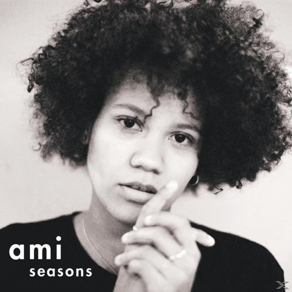 Ein Schwarzweißfoto einer Frau mit lockigem Haar, die in die Kamera blickt, mit „ami seasons“ am unteren Rand.