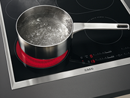 Table de cuisson à induction noire et argentée avec une casserole d'eau bouillante.