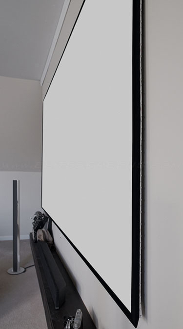Eine große weiße Projektionsleinwand mit schwarzem Rand ist an einer weißen Wand montiert. Darunter befinden sich eine Soundbar und andere Geräte.