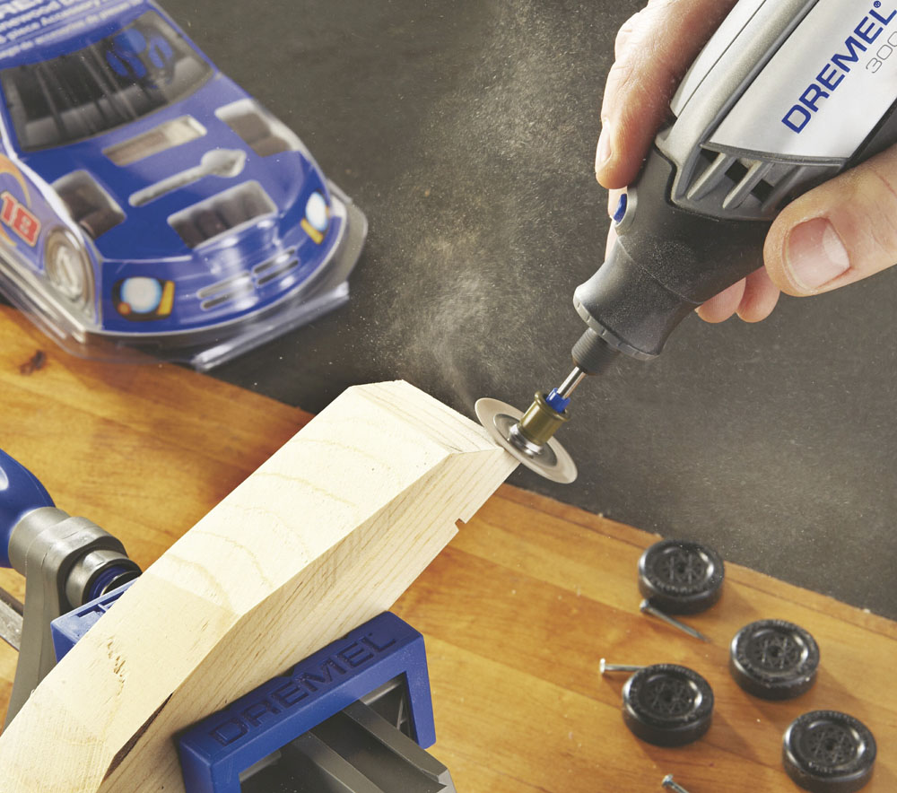 Dremel szerszám faanyagot vág, egy játékautó és más szerszámok mellett.