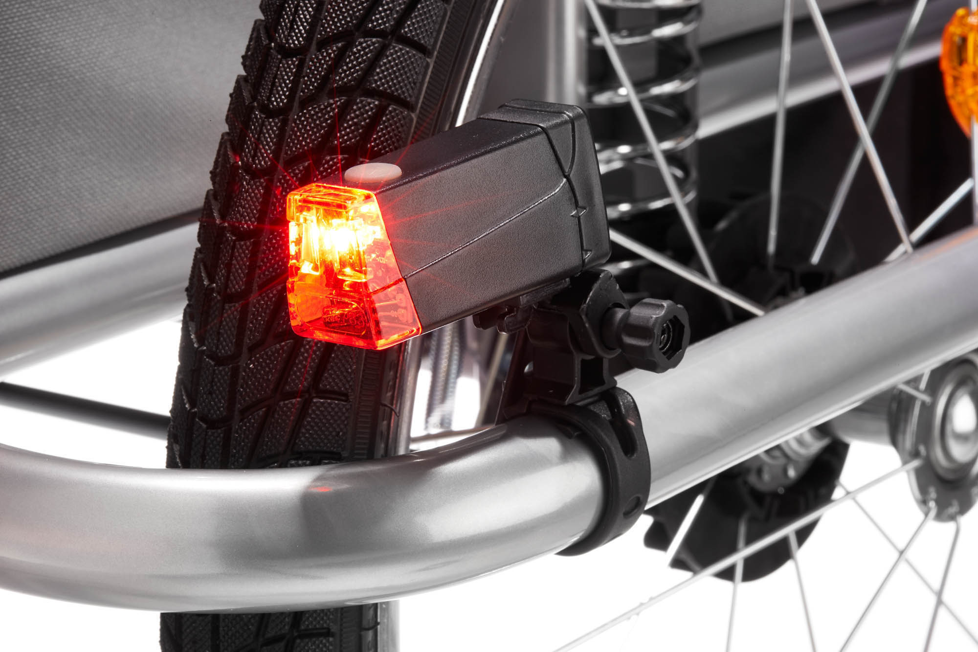 Nahaufnahme eines Fahrradanhänger-Rücklichts, rot und schwarz, an einem Metallrahmen befestigt.