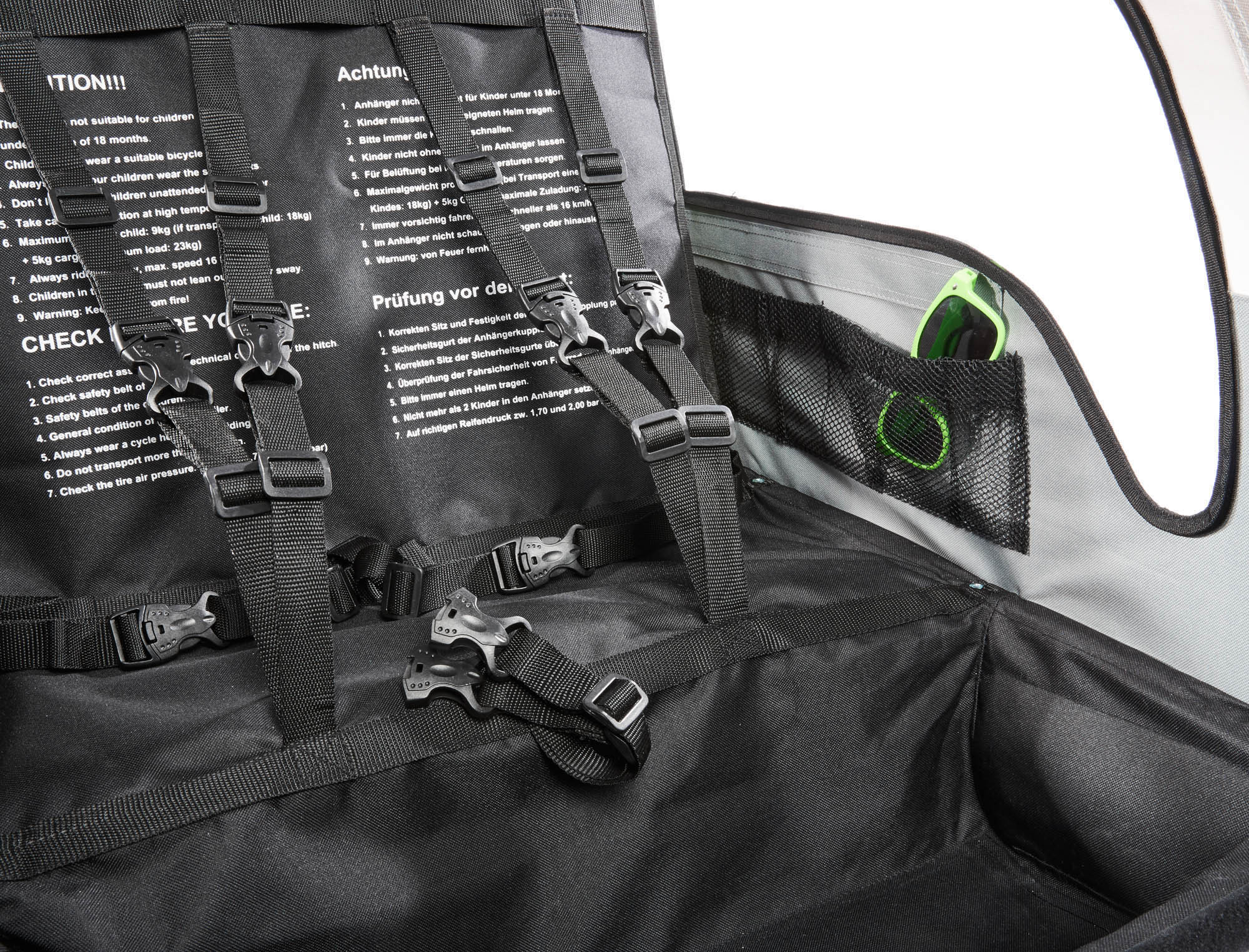 Nahaufnahme eines schwarz-grauen Fahrradanhänger-Innenraums mit Gurten, Schnallen und einer Tasche mit Sonnenbrille.