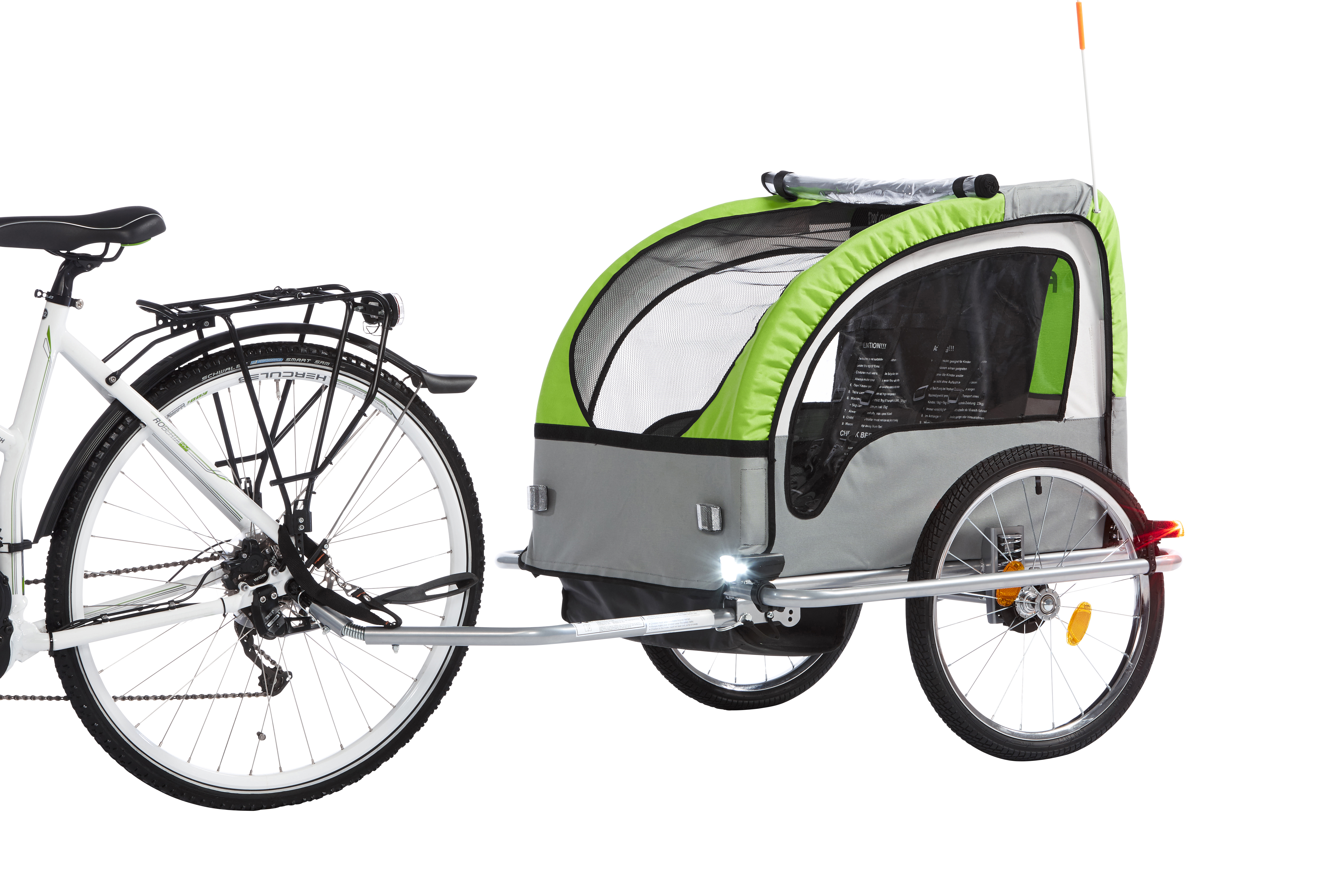 Fahrrad mit grün-grauem Anhänger. Anhänger hat zwei Räder, eine Flagge und ein Netzfenster.
