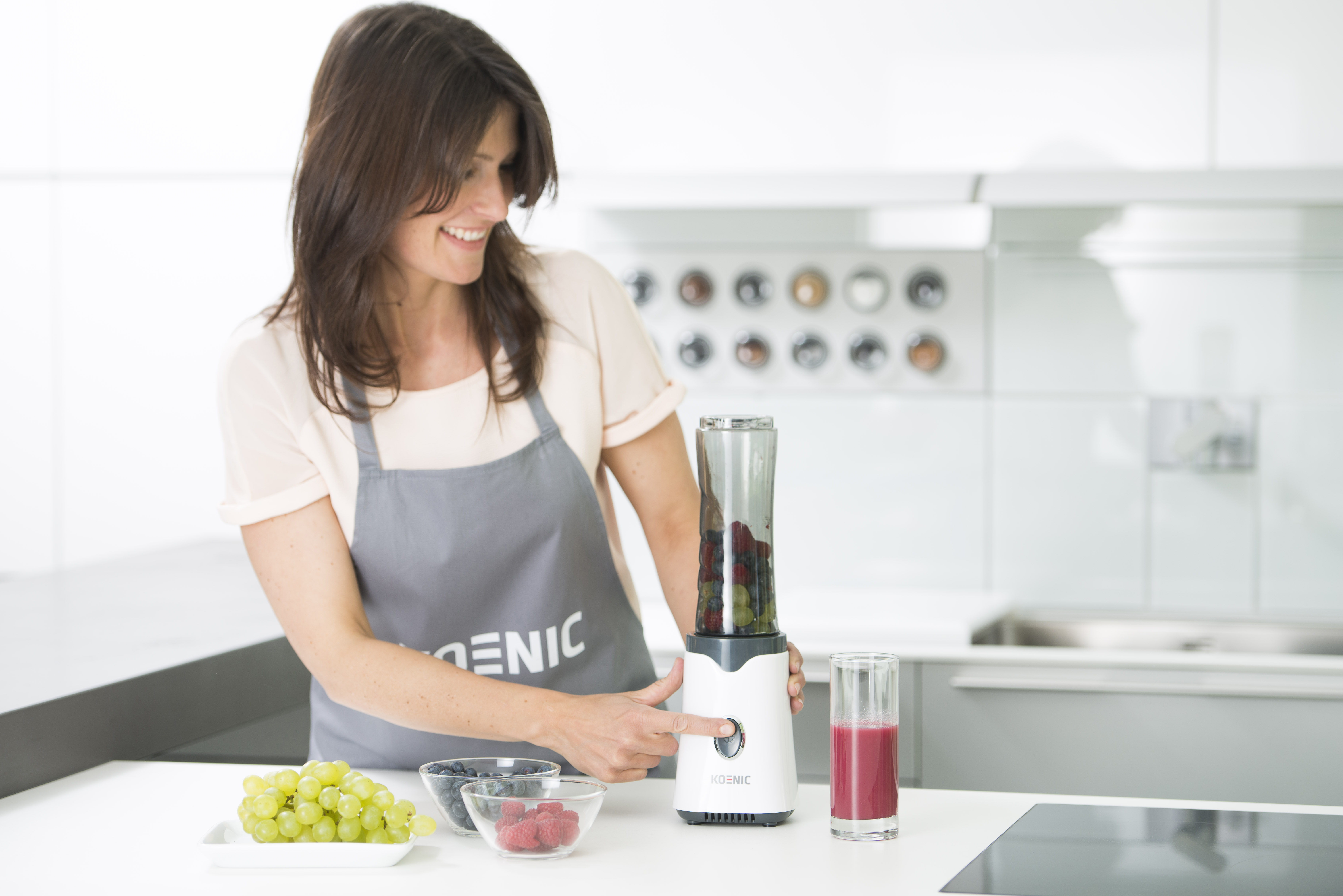 Frau macht Smoothie mit einem Mixer, Früchten und einem Glas.