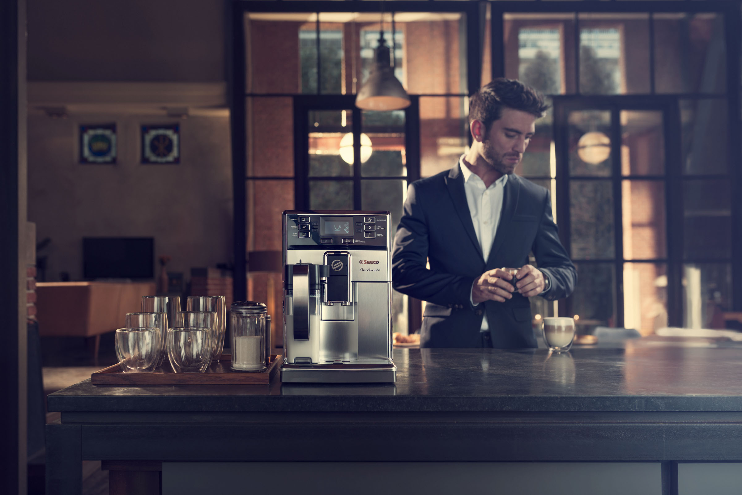 Mann in der Nähe einer Kaffeemaschine, hält eine Tasse. Ein häusliches Interieur.