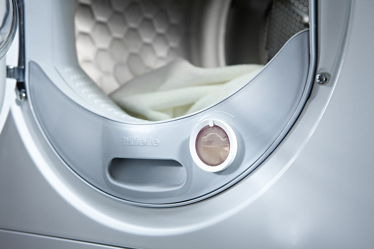 Close-up of a white washing machine door. A small compartment is open.